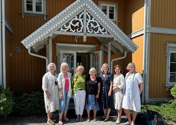 Syv damer står sammen foran inngangen til et gult, herskapelig hus.