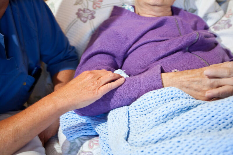 Sykepleier holder på armen til en eldre pasient i sengen